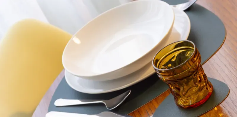 Una mesa puesta con platos blancos apilados, cubiertos y un vaso ámbar.