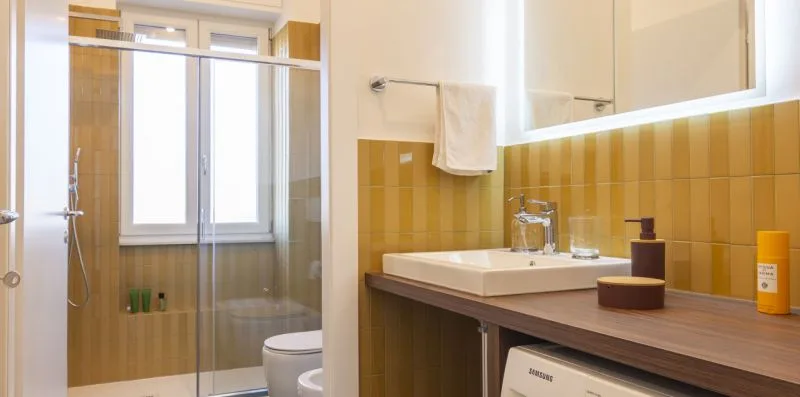 Un baño con ducha de vidrio, ventana y tocador.