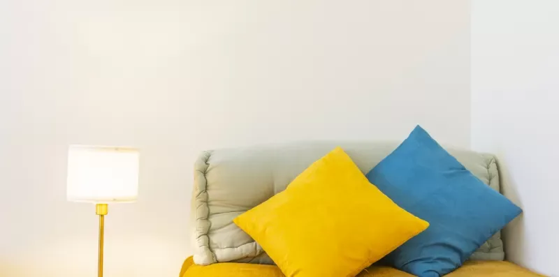 Una zona de asientos con cojines amarillos y azules junto a una lámpara de pie.