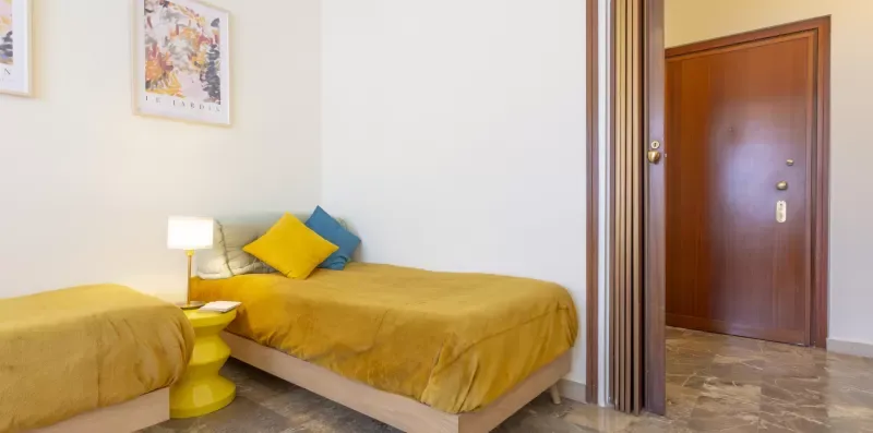 Un dormitorio con dos camas y una puerta de madera que da a una zona con suelo de baldosas.