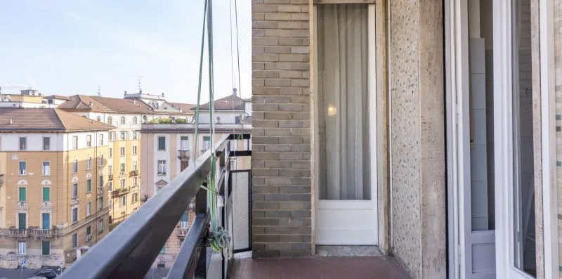 Un balcón estrecho con barandilla da a edificios de apartamentos vecinos.