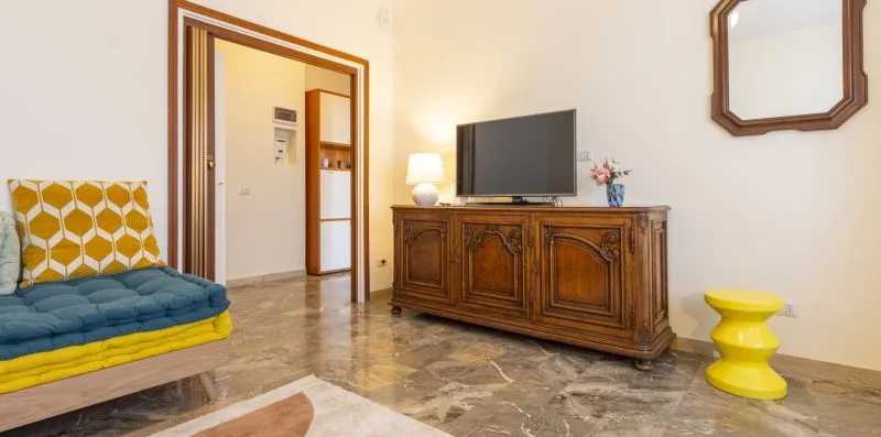 Una sala de estar con un televisor sobre un mueble de madera y asientos coloridos.