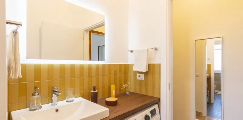 Un lavabo de baño con un espejo amplio, una pared de azulejos y una encimera de madera.