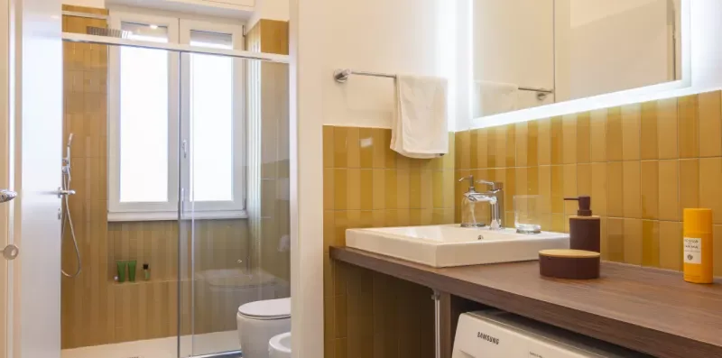 Un lavabo de baño está junto a una ducha de vidrio y una ventana.