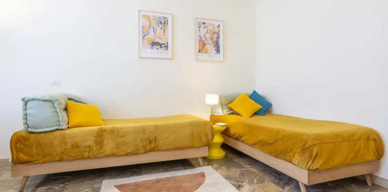 Dormitorio con dos camas individuales, ropa de cama amarilla y cuadros enmarcados.