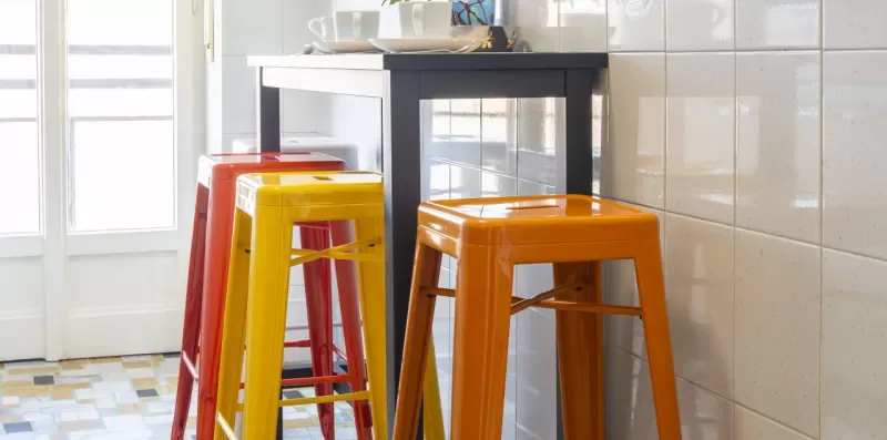 Una luminosa zona de comedor de cocina con taburetes de colores junto a una encimera.