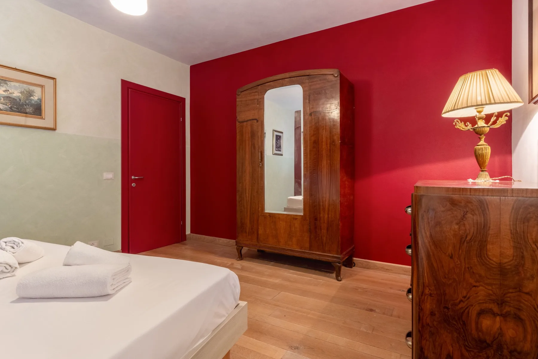 A bedroom with a bed, a wooden wardrobe, and a red accent wall.