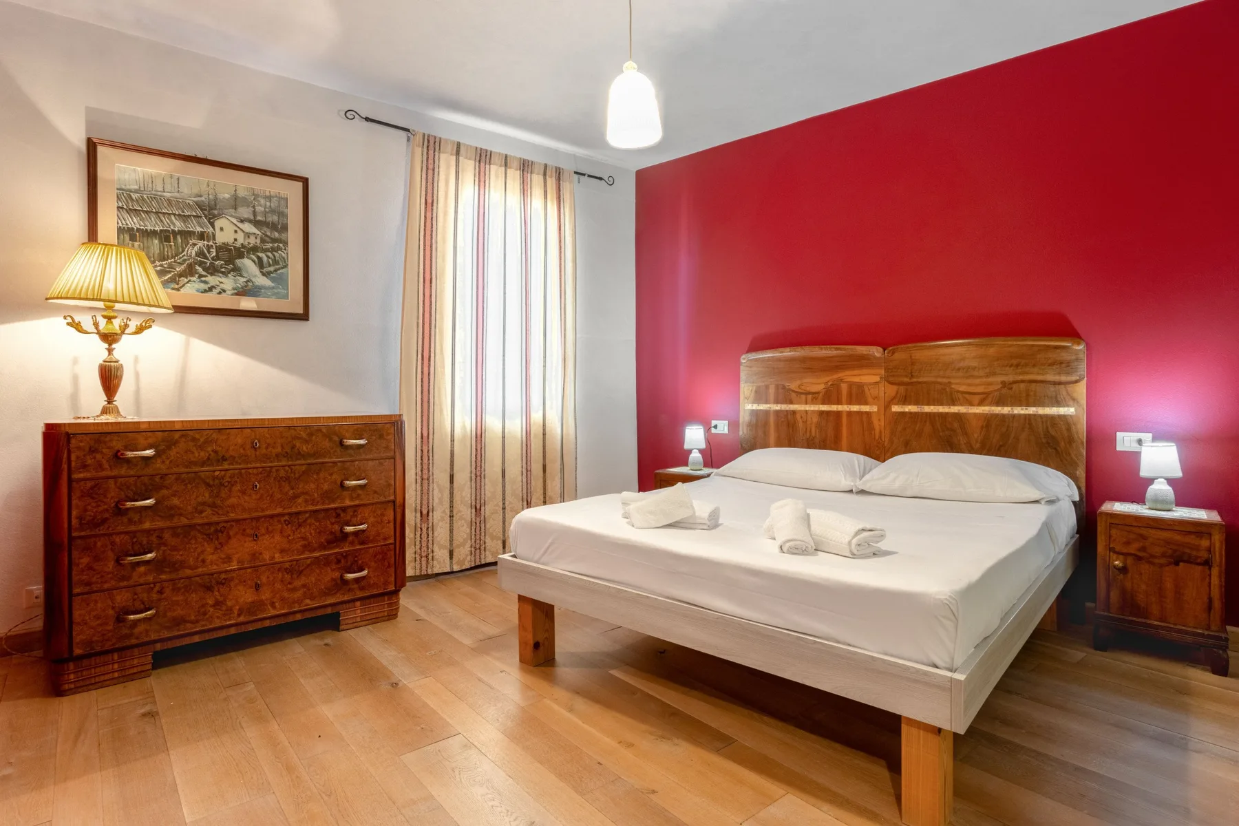 A bedroom with a double bed, wooden dresser, and red accent wall.