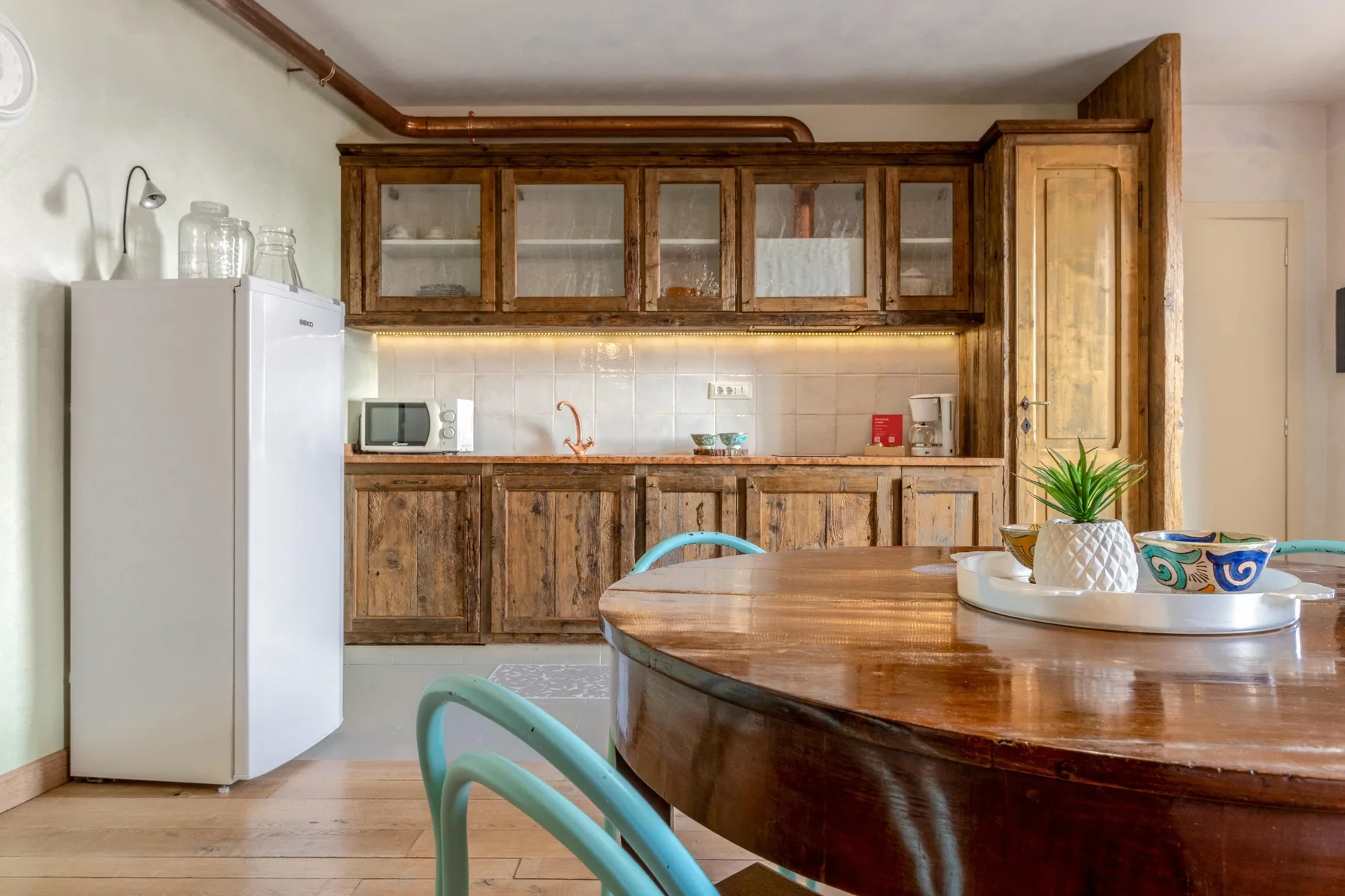 A kitchen with wooden cabinets, a refrigerator, and a rounded dining table.
