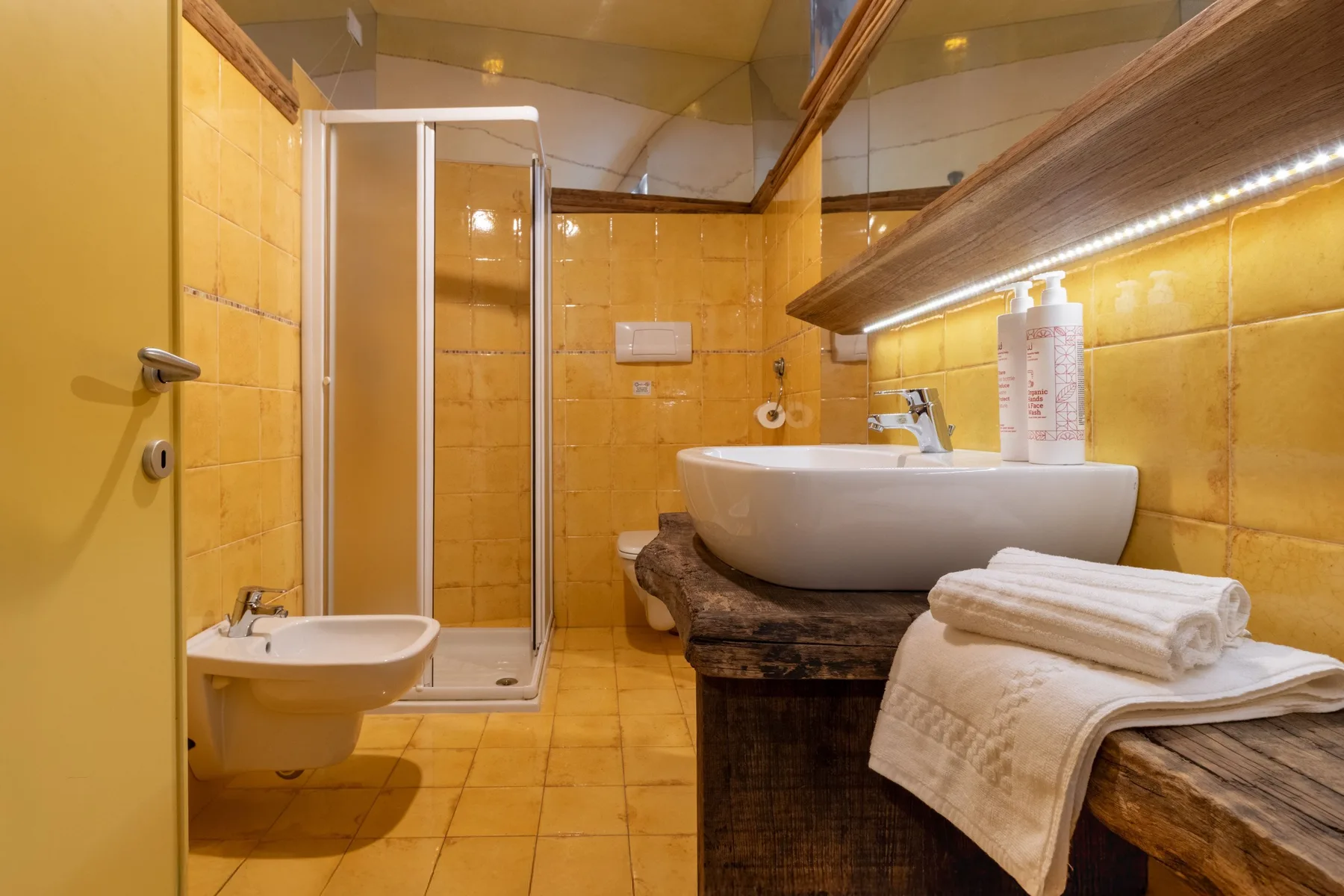 A tiled bathroom with a shower, bidet, and sink on a wooden counter.
