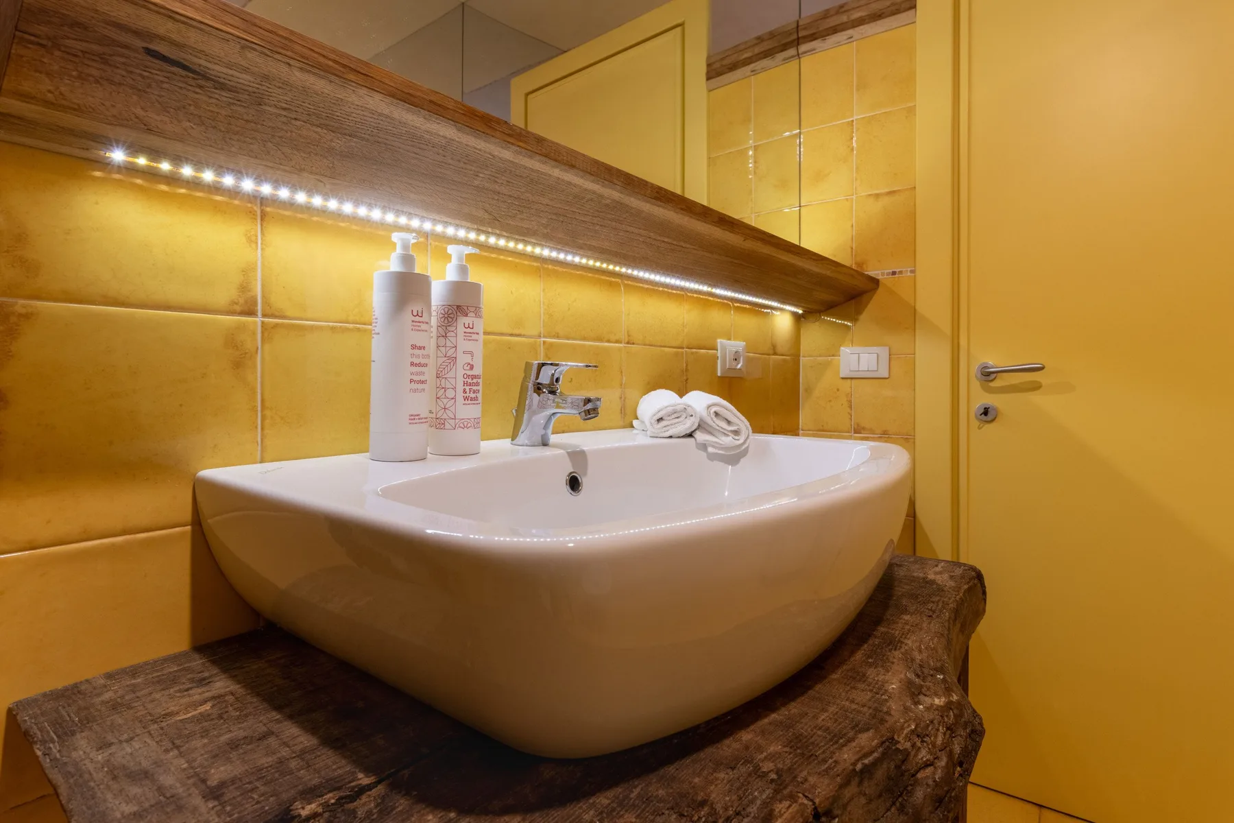 A bathroom sink sits beneath a wide mirror, with toiletries and folded towels nearby.