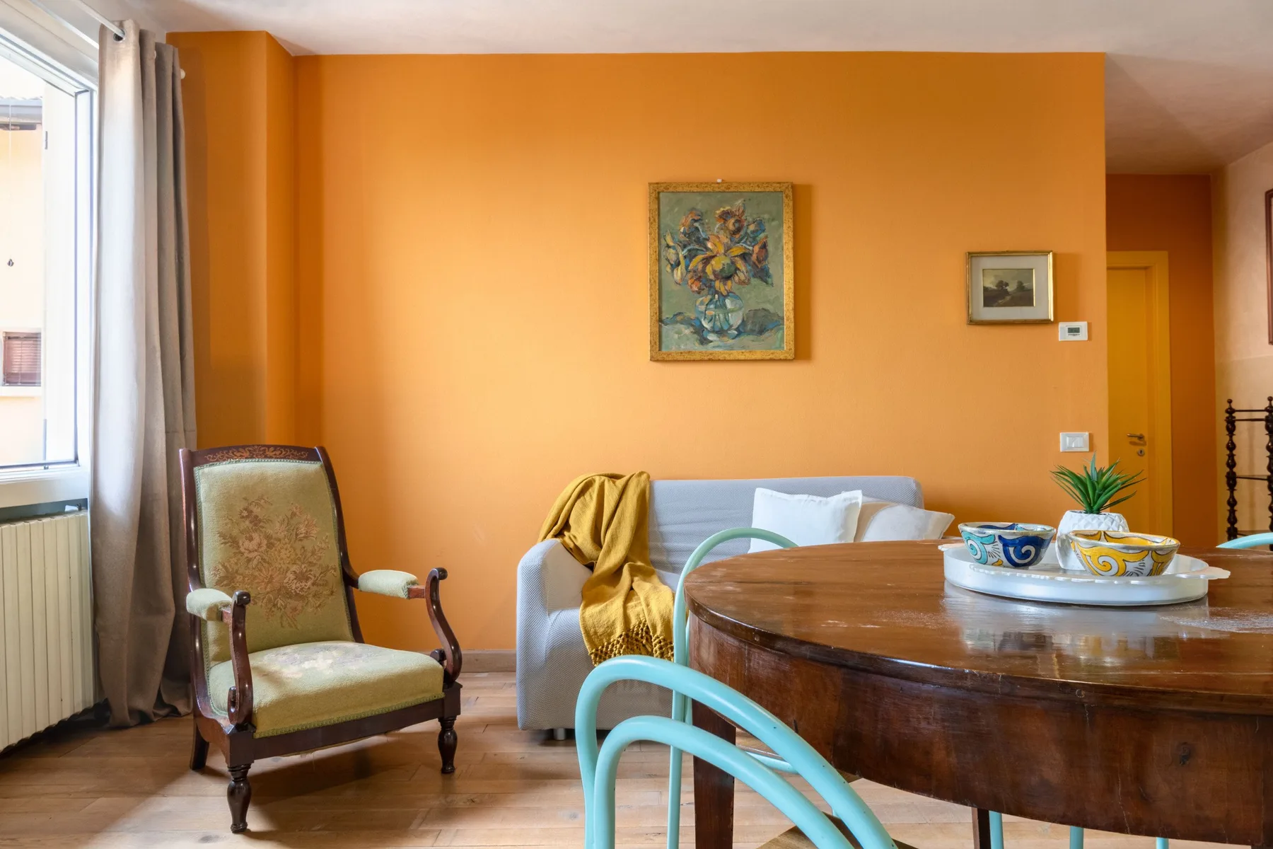An orange-walled living and dining area with seating and a round wooden table.