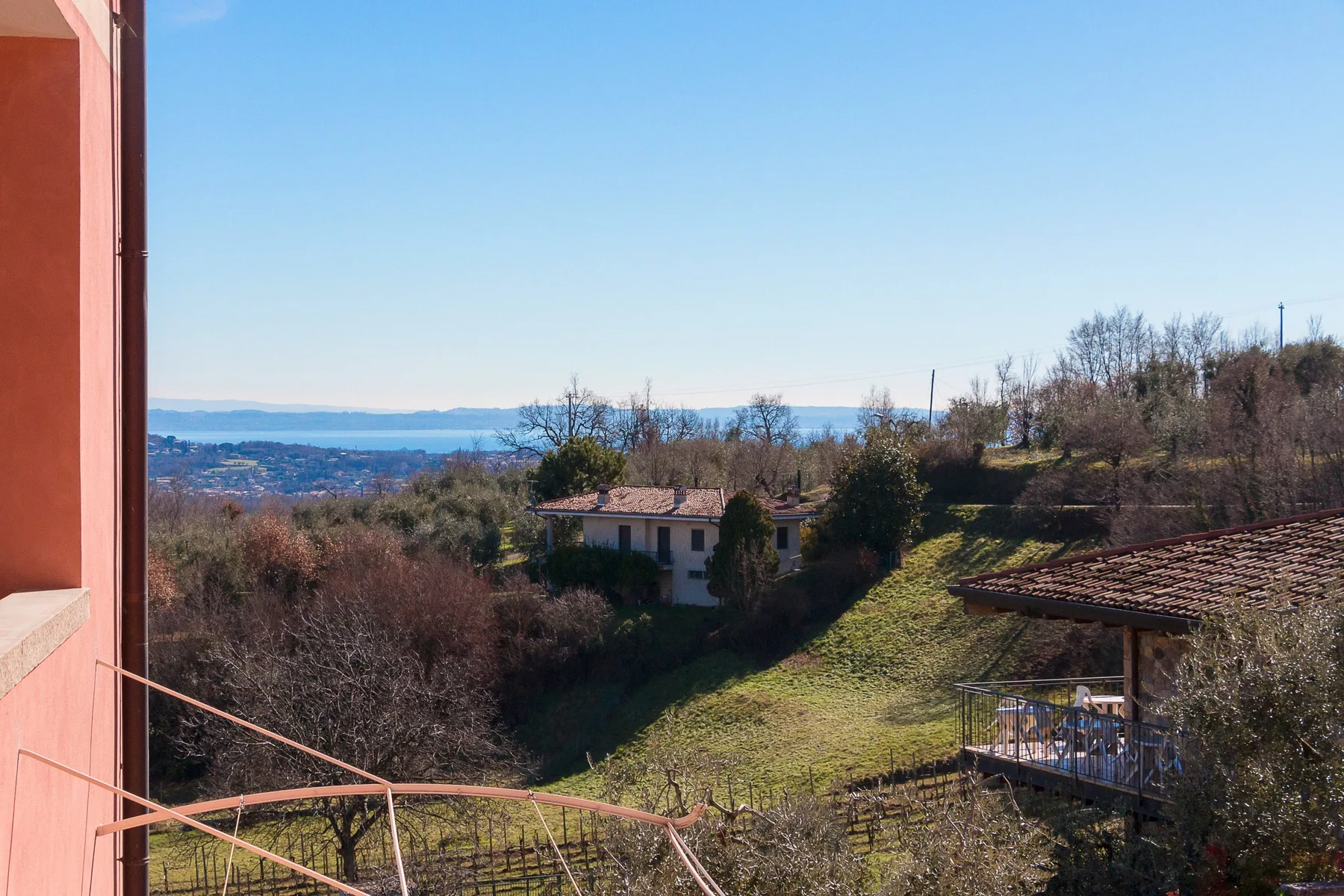 A hillside view overlooks a small house, leafless trees, and distant water.