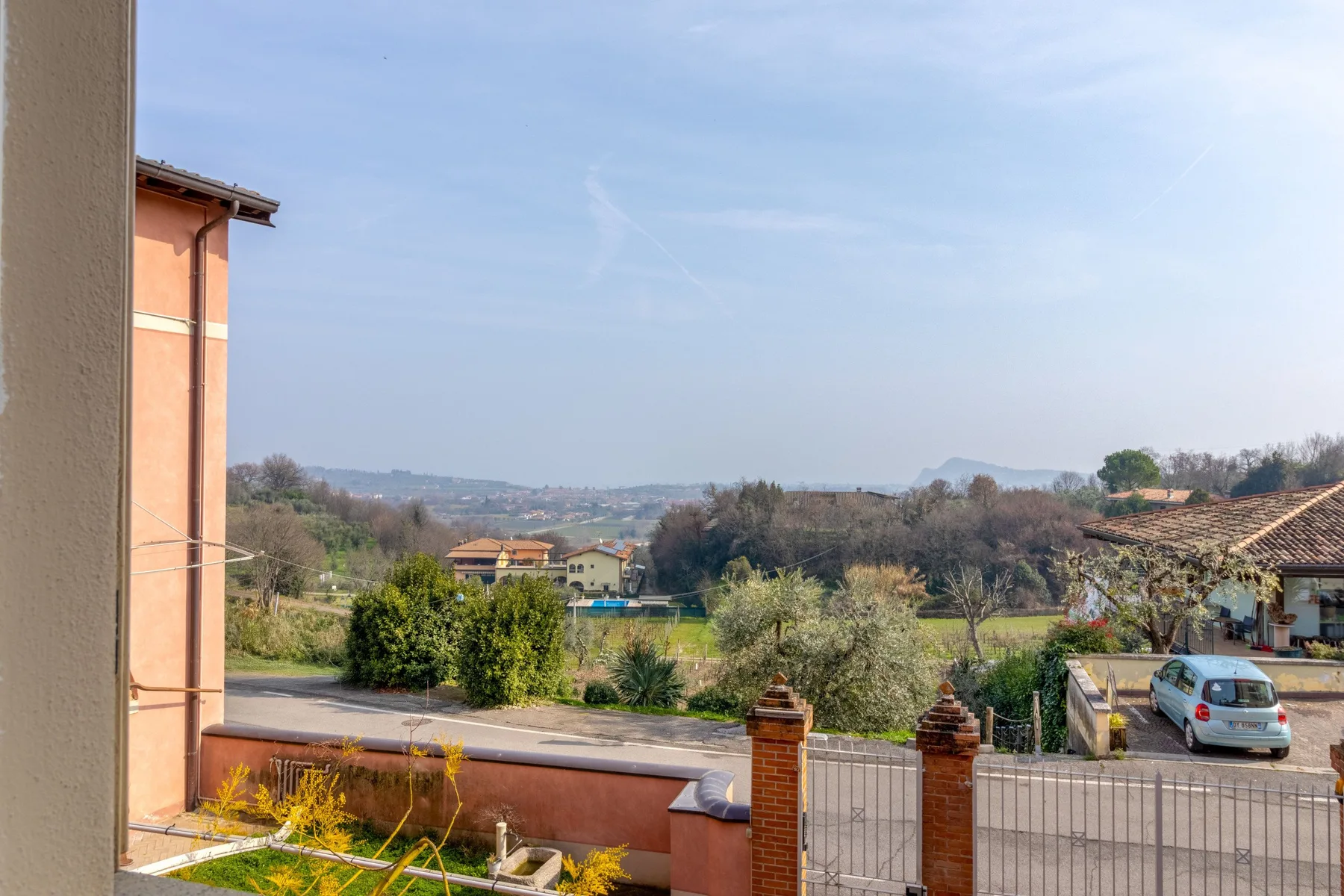 A countryside view from a terrace overlooks gardens, trees, and distant hills.