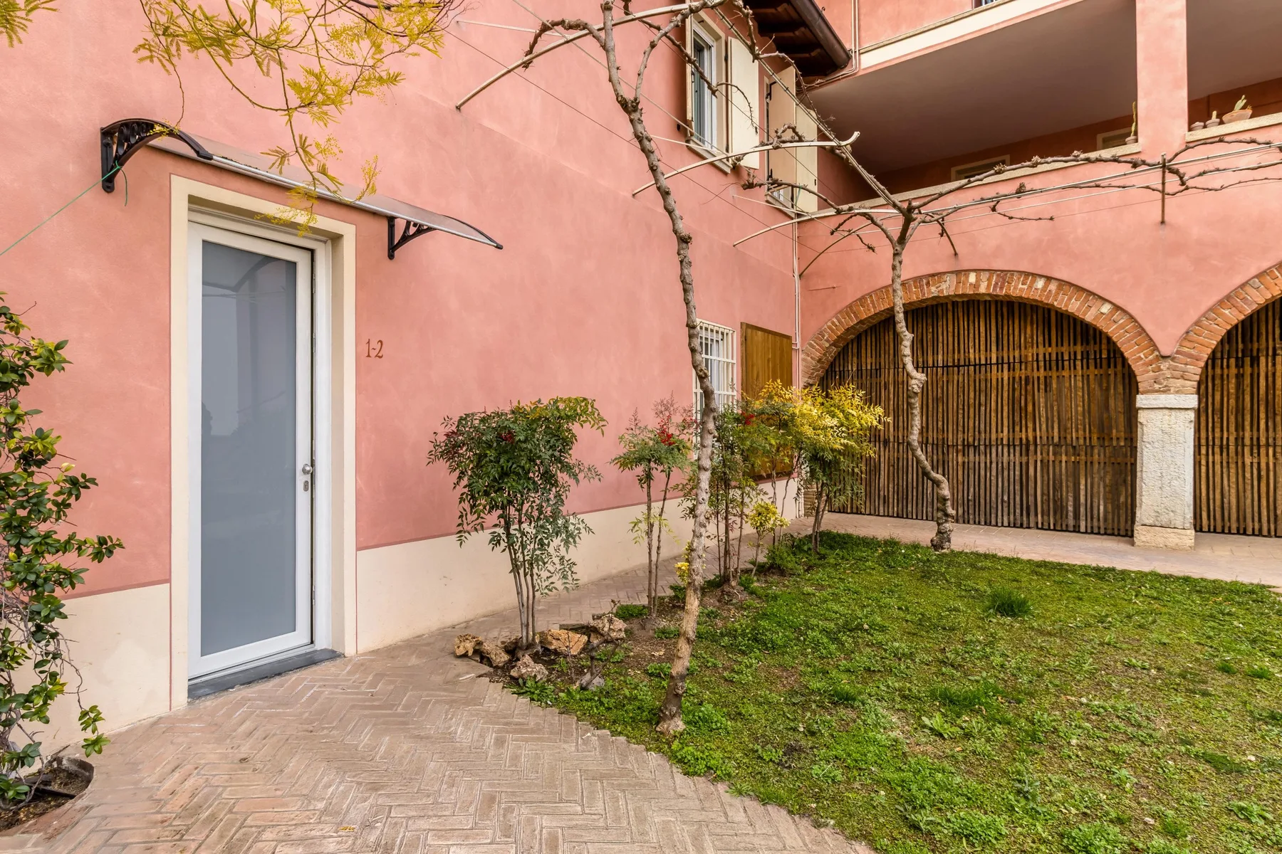 A pink stucco building faces a small courtyard with grass and a paved path.