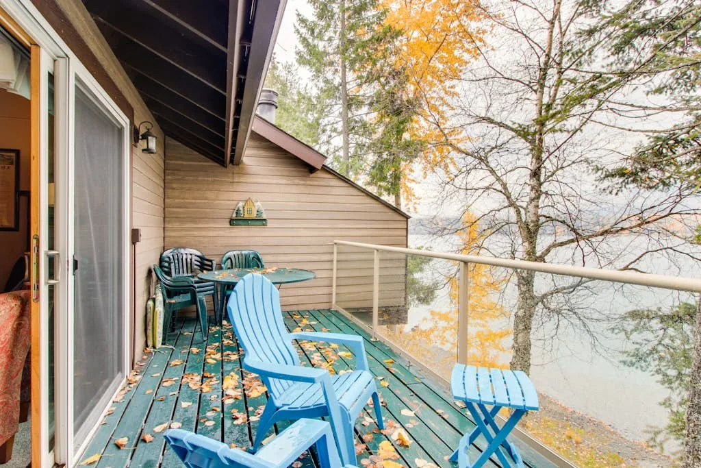 A lakeside deck with blue seating overlooks the water and autumn trees.