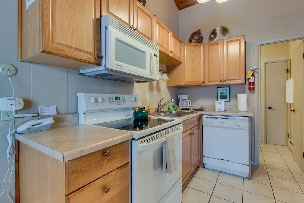A compact kitchen with wooden cabinets, an electric range, and a dishwasher.