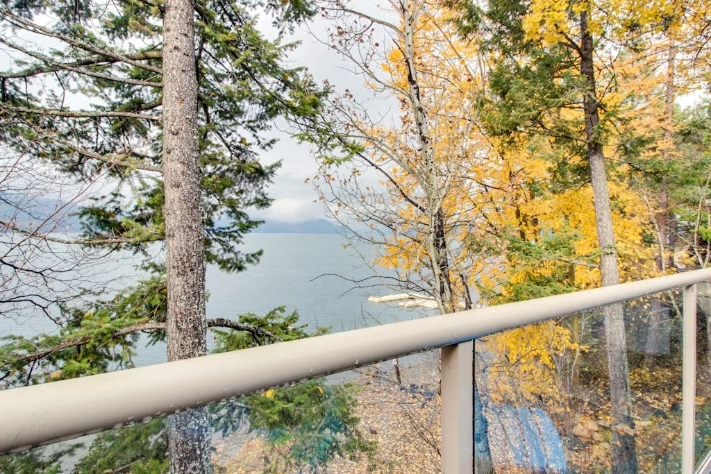 A balcony railing overlooks a lake framed by trees with autumn foliage.