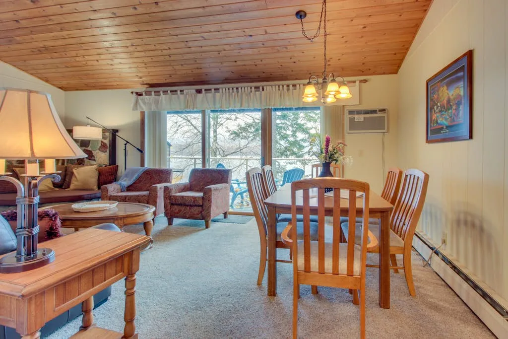 A living and dining room with wooden seating and large windows.