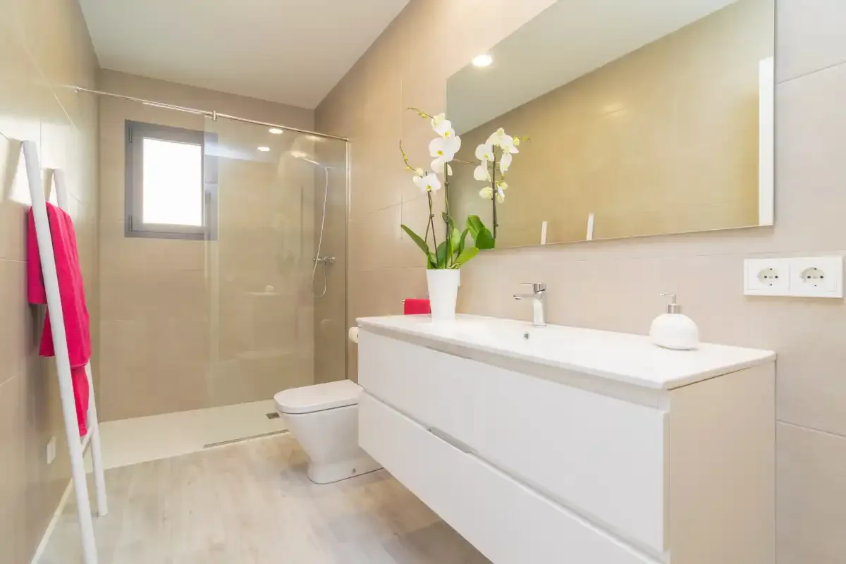 Un baño luminoso con ducha de vidrio, inodoro y un amplio lavabo.