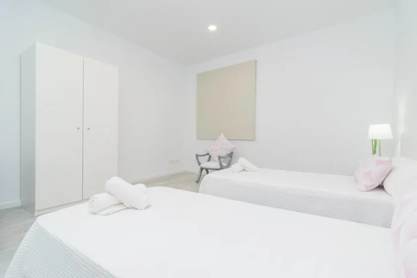 Un dormitorio luminoso con dos camas y un armario.