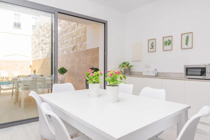 Un comedor luminoso con una mesa blanca junto a grandes puertas de cristal.