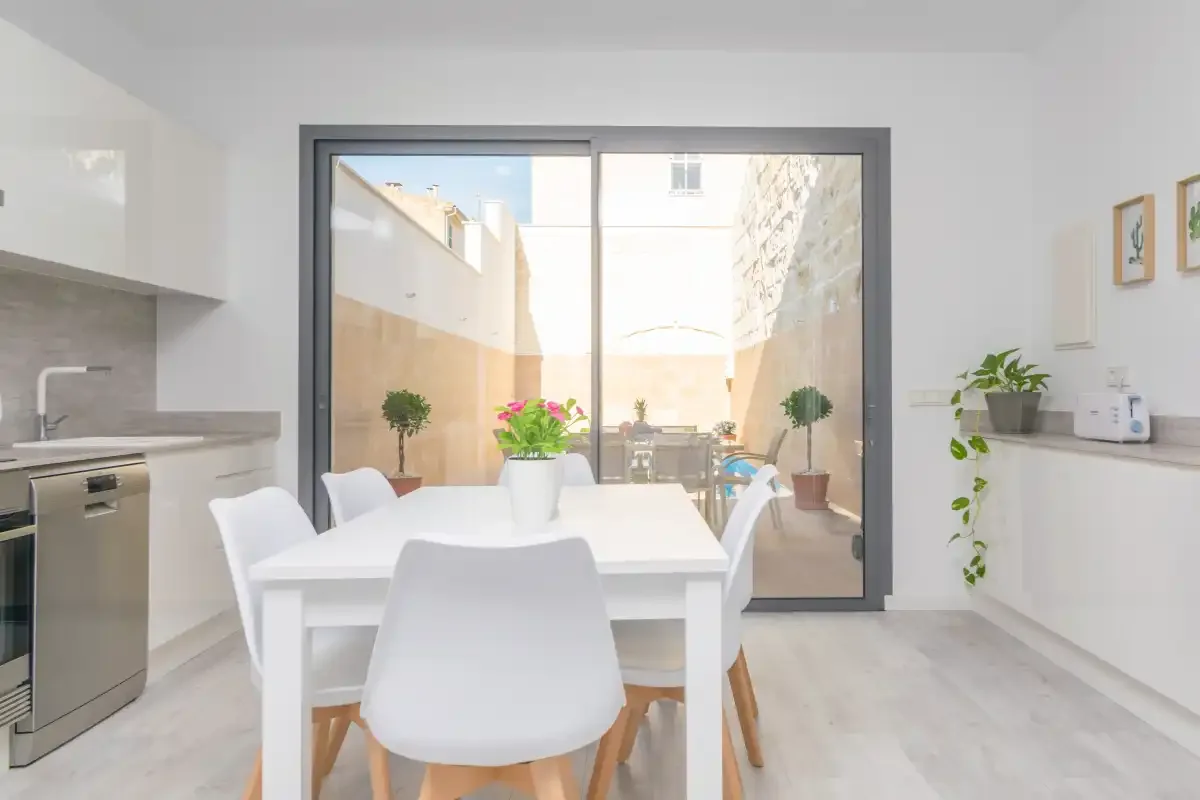 Un comedor luminoso con una mesa blanca junto a grandes puertas de vidrio que dan a un patio.