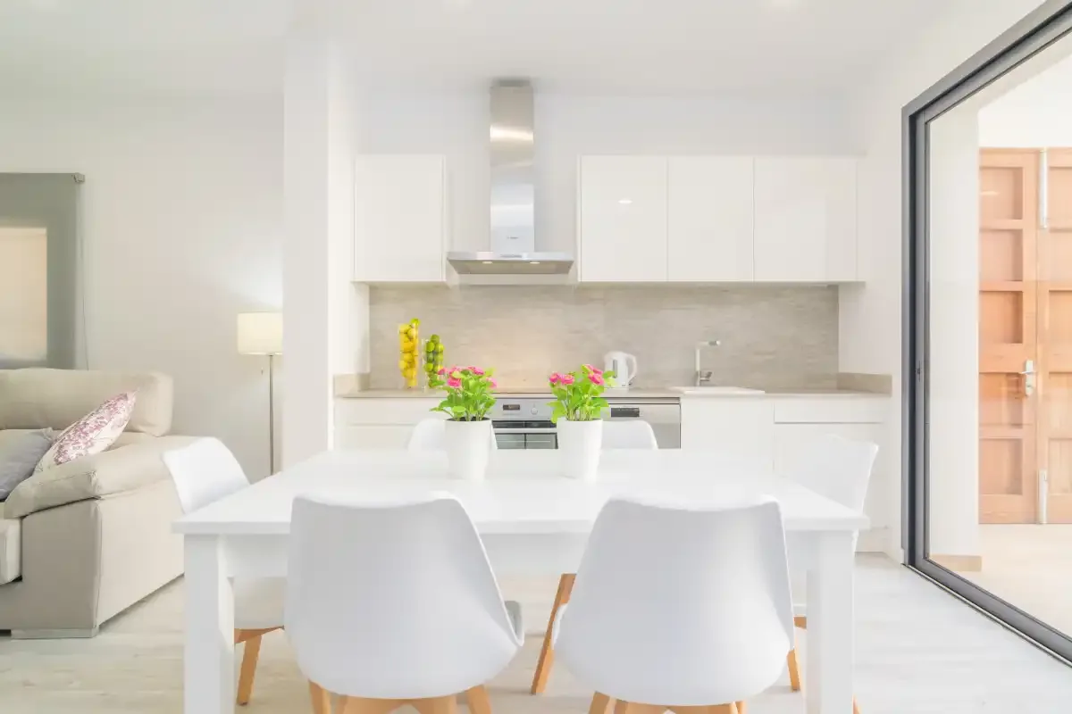 Un comedor luminoso con una mesa blanca y una cocina abierta al fondo.