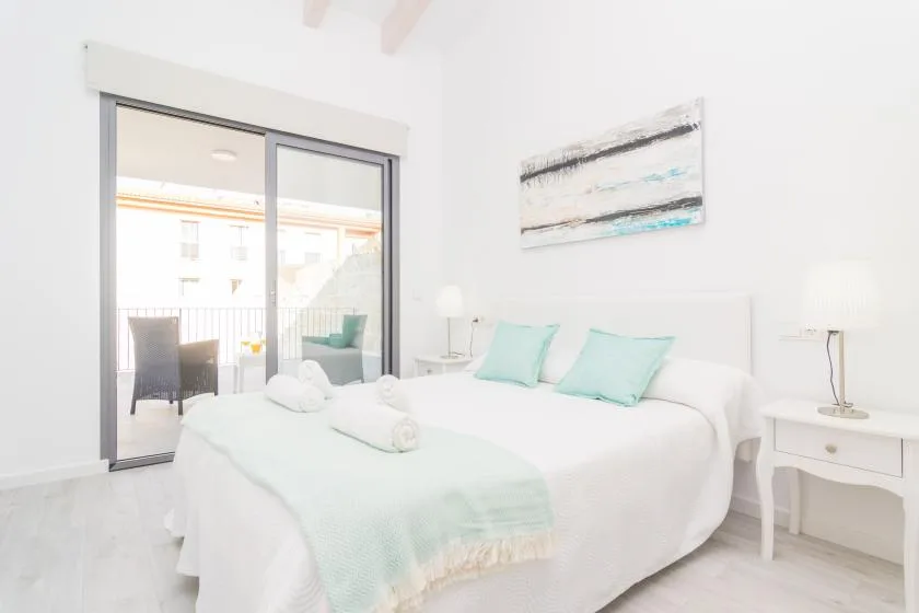 Un dormitorio luminoso con una cama bien tendida y puertas corredizas de vidrio a un balcón.