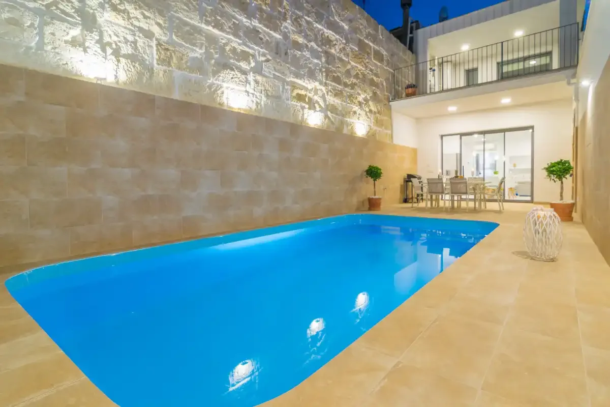 Una piscina azul está junto a un muro de piedra y una zona de comedor.
