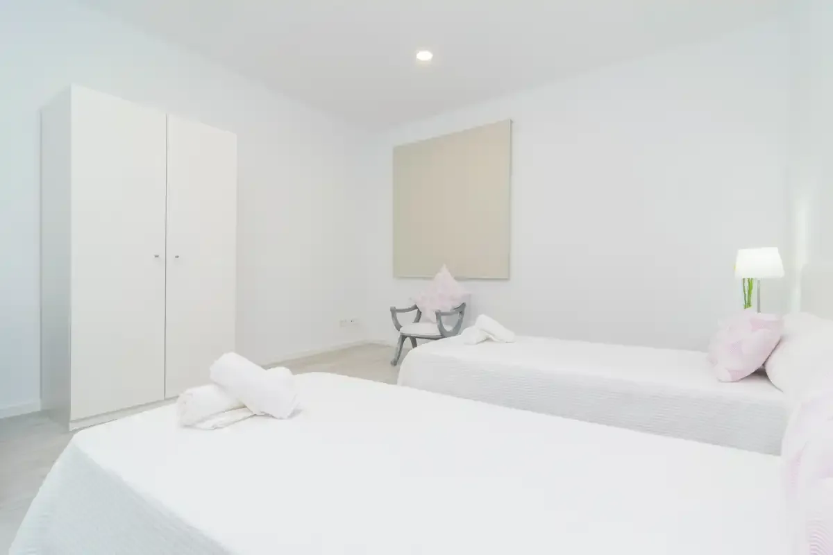 Un dormitorio luminoso con dos camas, ropa de cama blanca y un armario.