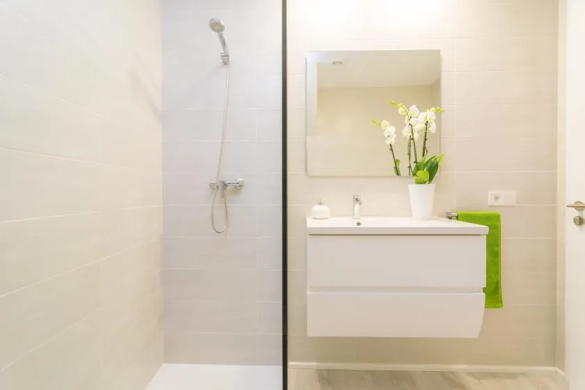 Un baño luminoso con una mampara de vidrio y un lavabo bajo un espejo.