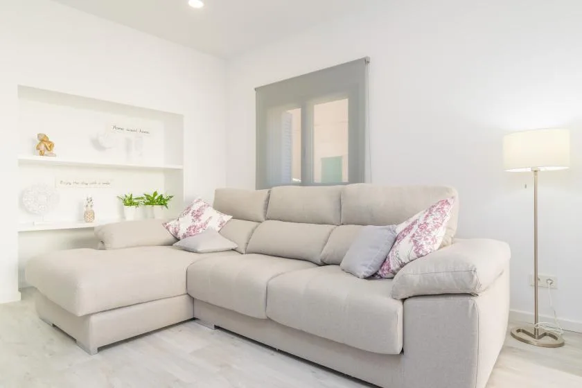 Una sala luminosa con un sofá seccional claro y una lámpara de pie.