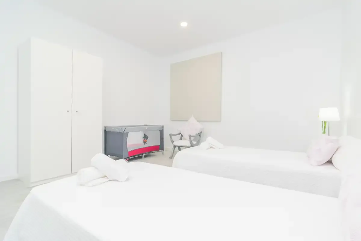 Un dormitorio blanco y luminoso con dos camas, un armario y un televisor.