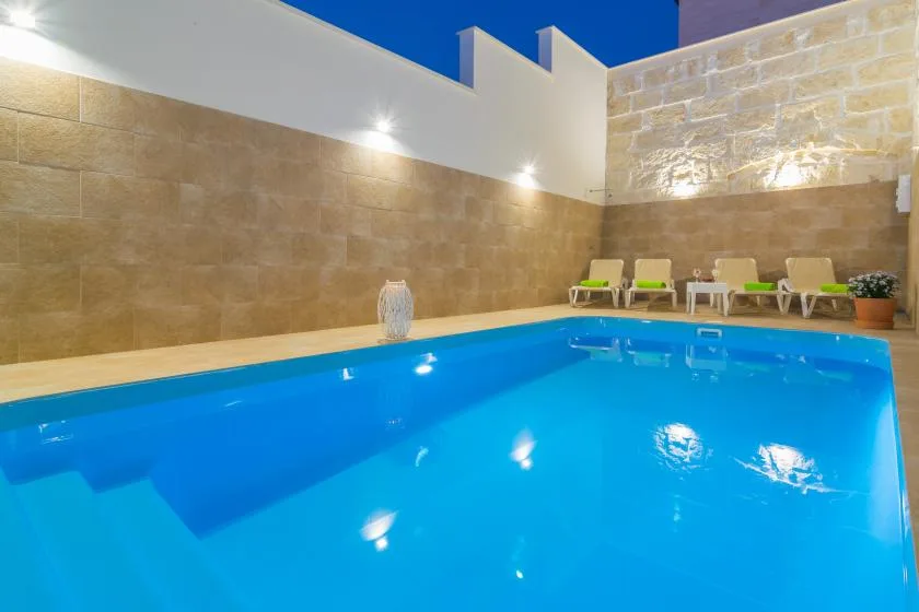 Una piscina azul brillante está junto a una pared revestida de piedra y asientos.