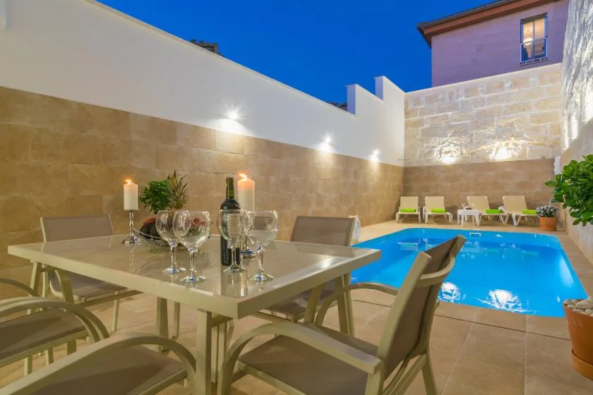 Una zona de comedor al aire libre junto a una piscina iluminada.