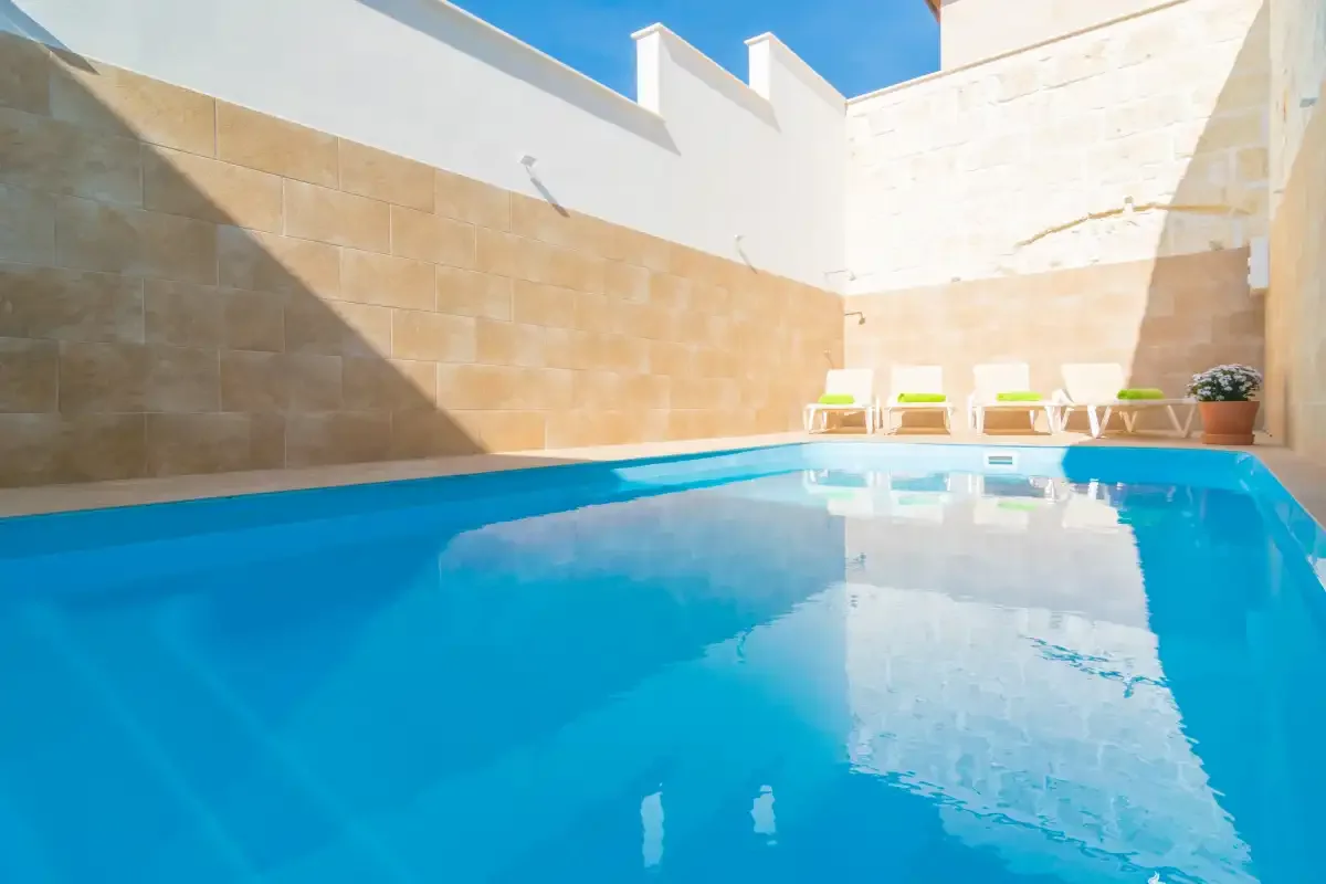 Una piscina está junto a muros altos, con tumbonas al fondo.