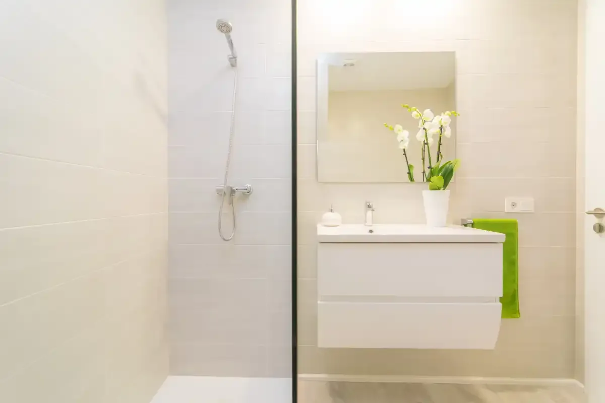 Un baño luminoso con lavabo suspendido, espejo y ducha.