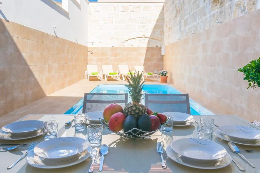 Una mesa puesta con platos y fruta da a una pequeña piscina en el patio.