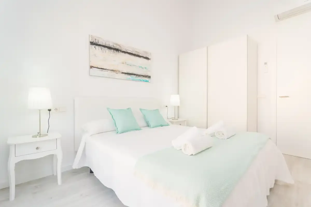 Un dormitorio luminoso con una cama vestida de blanco y ropa de cama verde menta pálido.