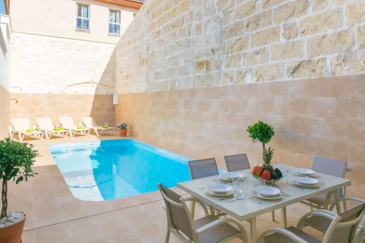 Una piscina en un patio junto a una mesa de comedor y asientos al aire libre.