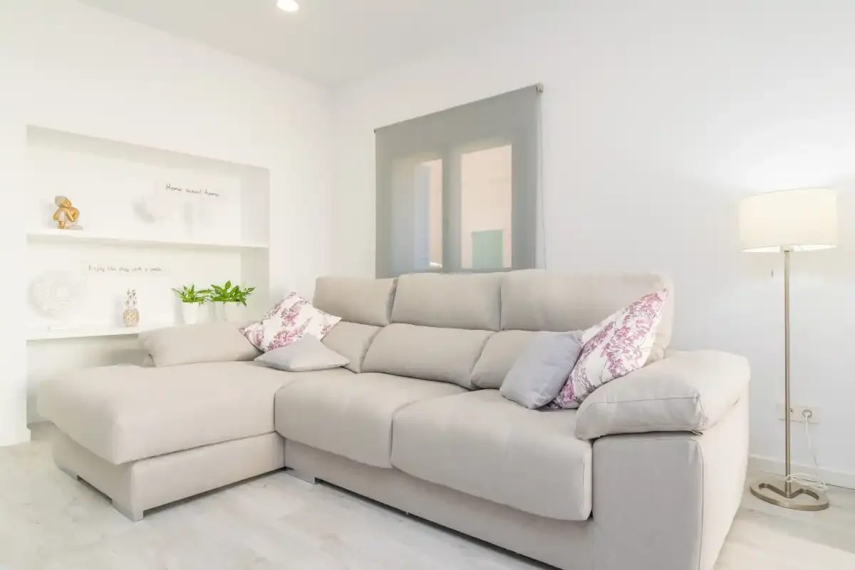 Una sala de estar luminosa con un sofá seccional claro y una lámpara de pie.