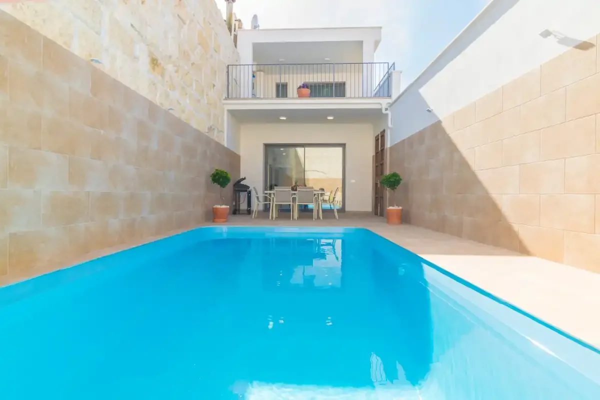 Una piscina luminosa en el patio está frente a una casa moderna.