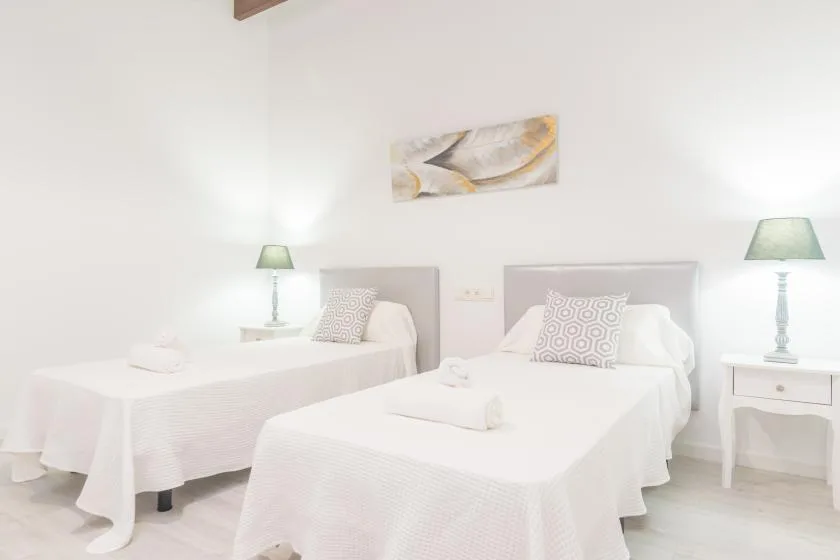 Un dormitorio luminoso con dos camas vestidas con ropa de cama blanca.