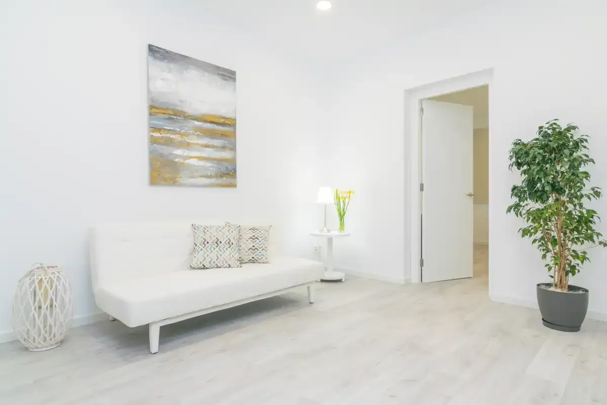Una sala de estar luminosa con un sofá blanco y una planta en maceta.