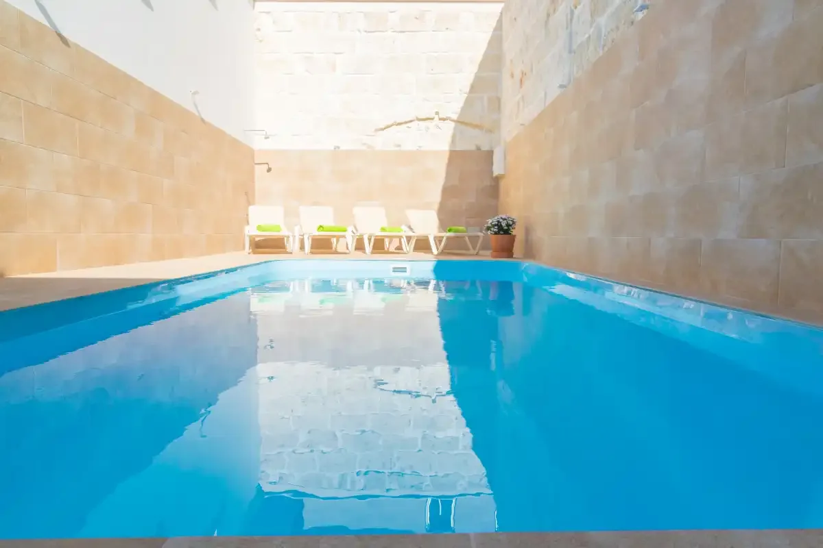 Una piscina se encuentra en un patio soleado rodeado de muros de piedra.