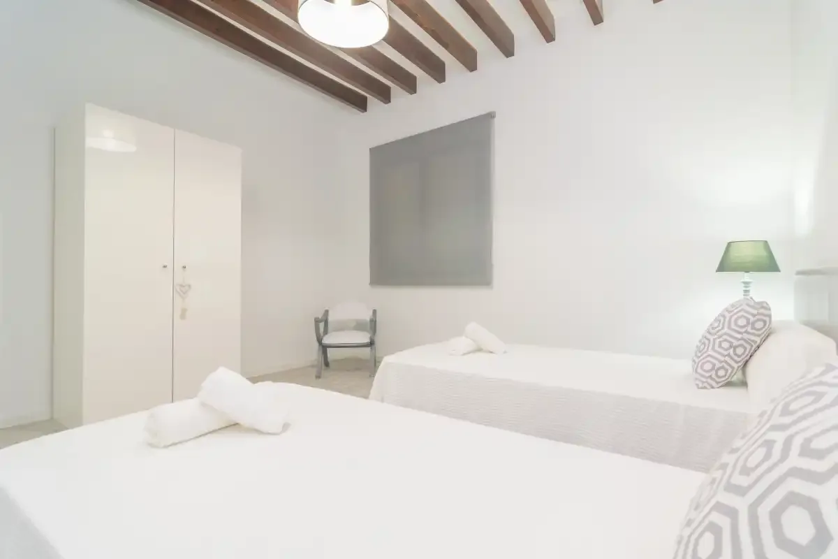 Un dormitorio luminoso con dos camas, un armario y vigas de techo vistas.