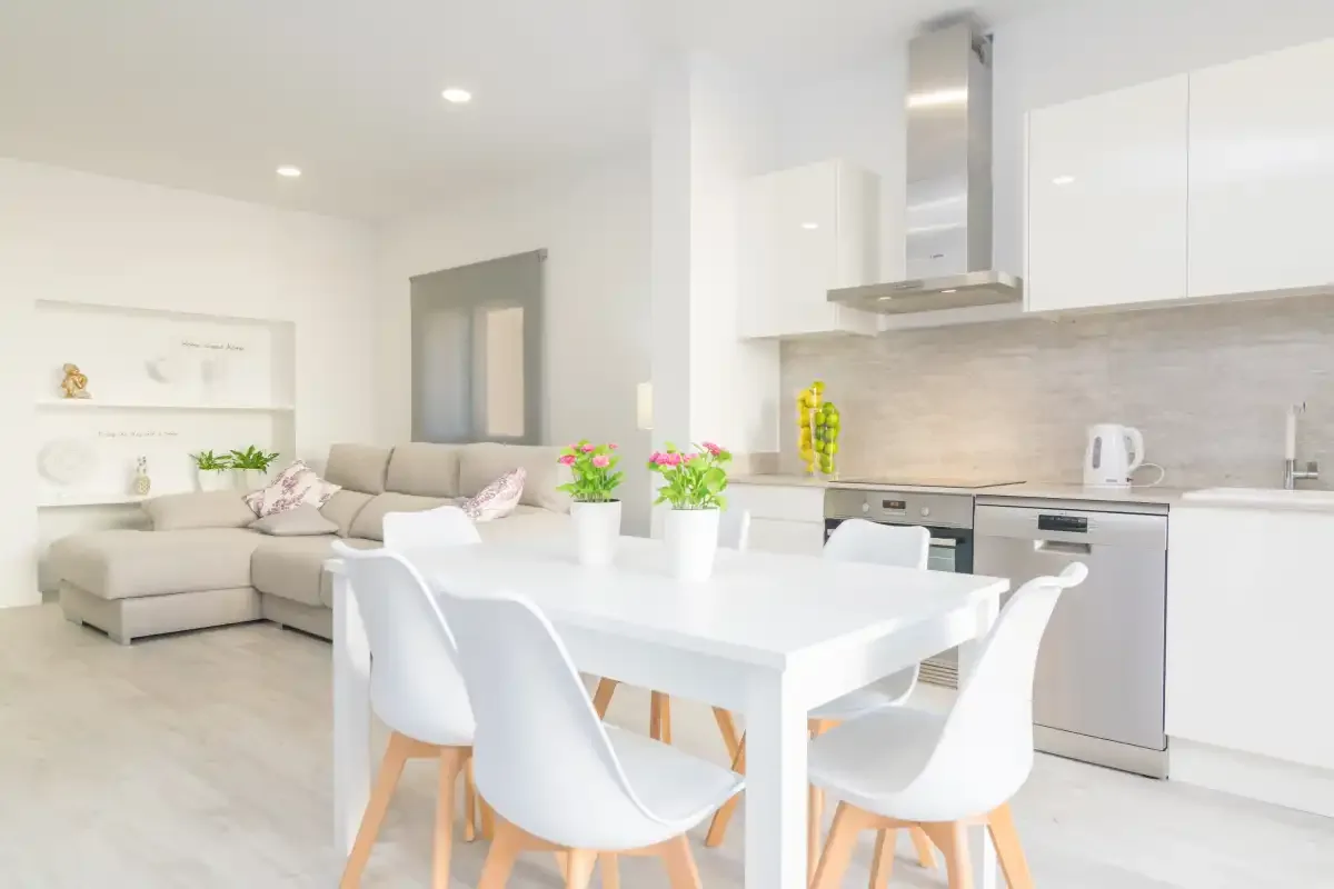 Una zona abierta de estar y comedor con una mesa blanca junto a una cocina moderna.