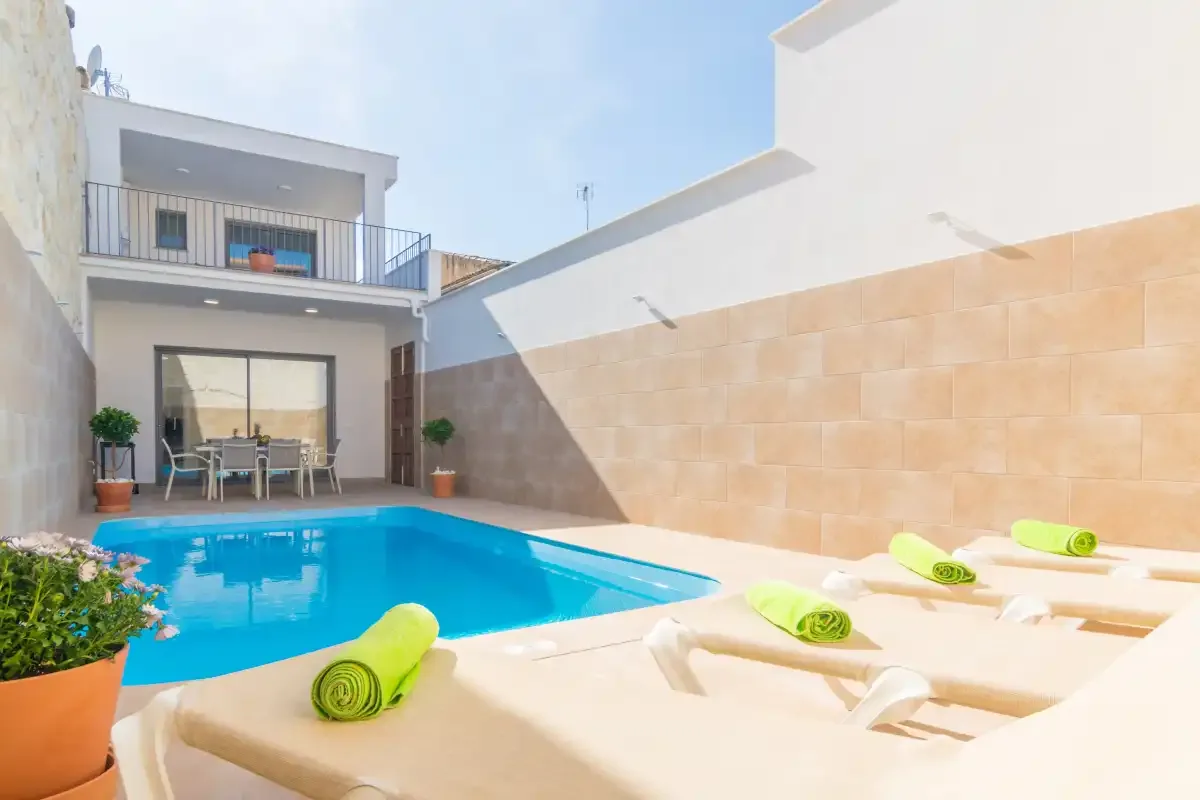 Una piscina soleada en un patio con tumbonas y toallas enrolladas.