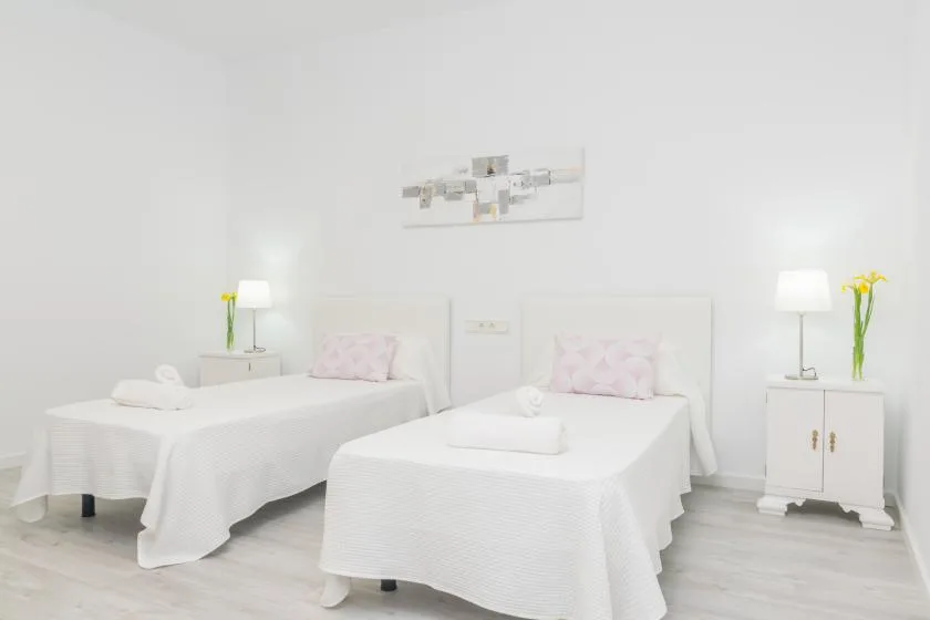 Un dormitorio luminoso con dos camas, mesitas de noche a juego y un cuadro sencillo.